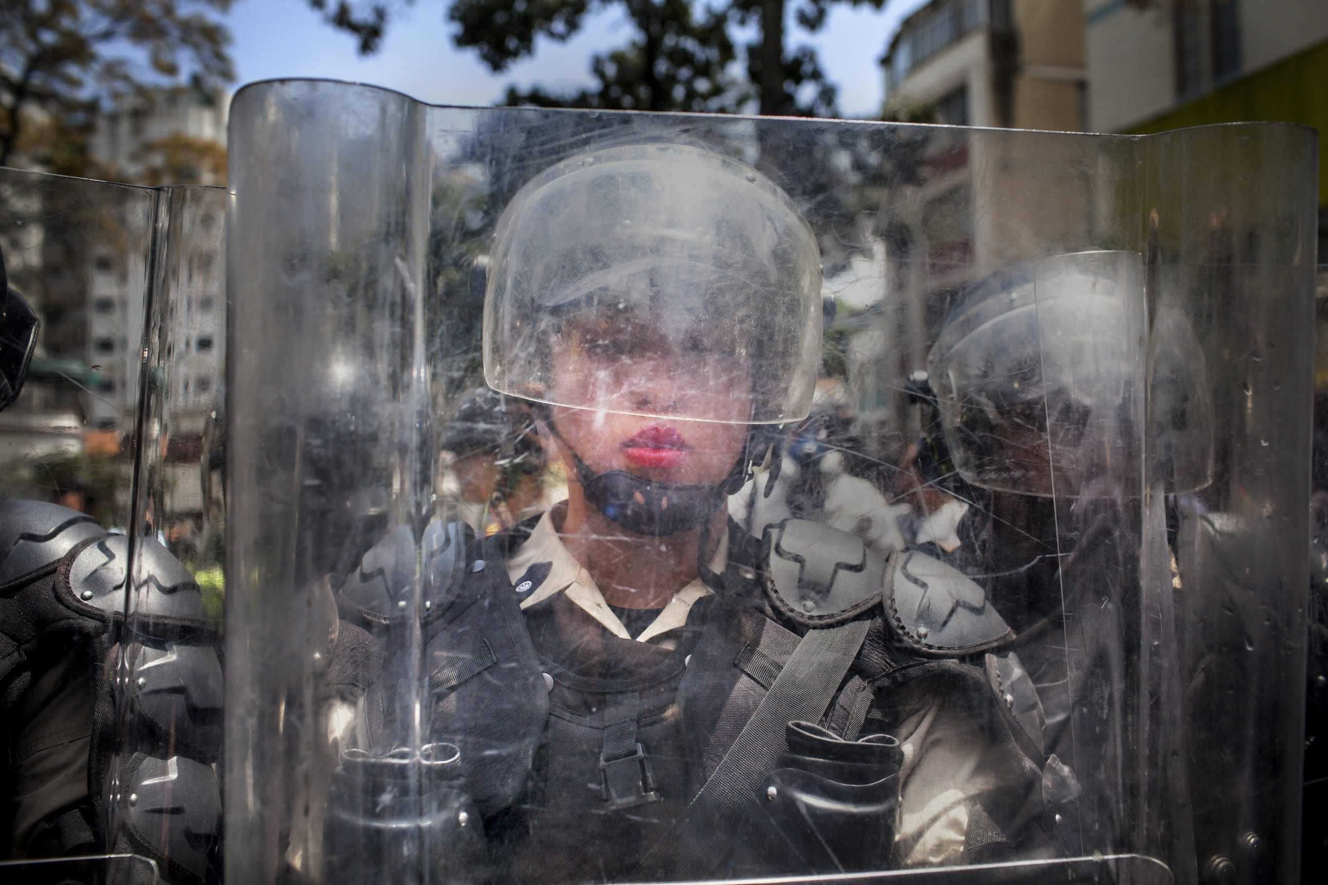 March 6th, 2014. Caracas, Venezuela. A National Police officer behind a riot shield is pushed backwards by a crush of demonstrators during the March of the Empty Pots, which coincided with International Women's Day.