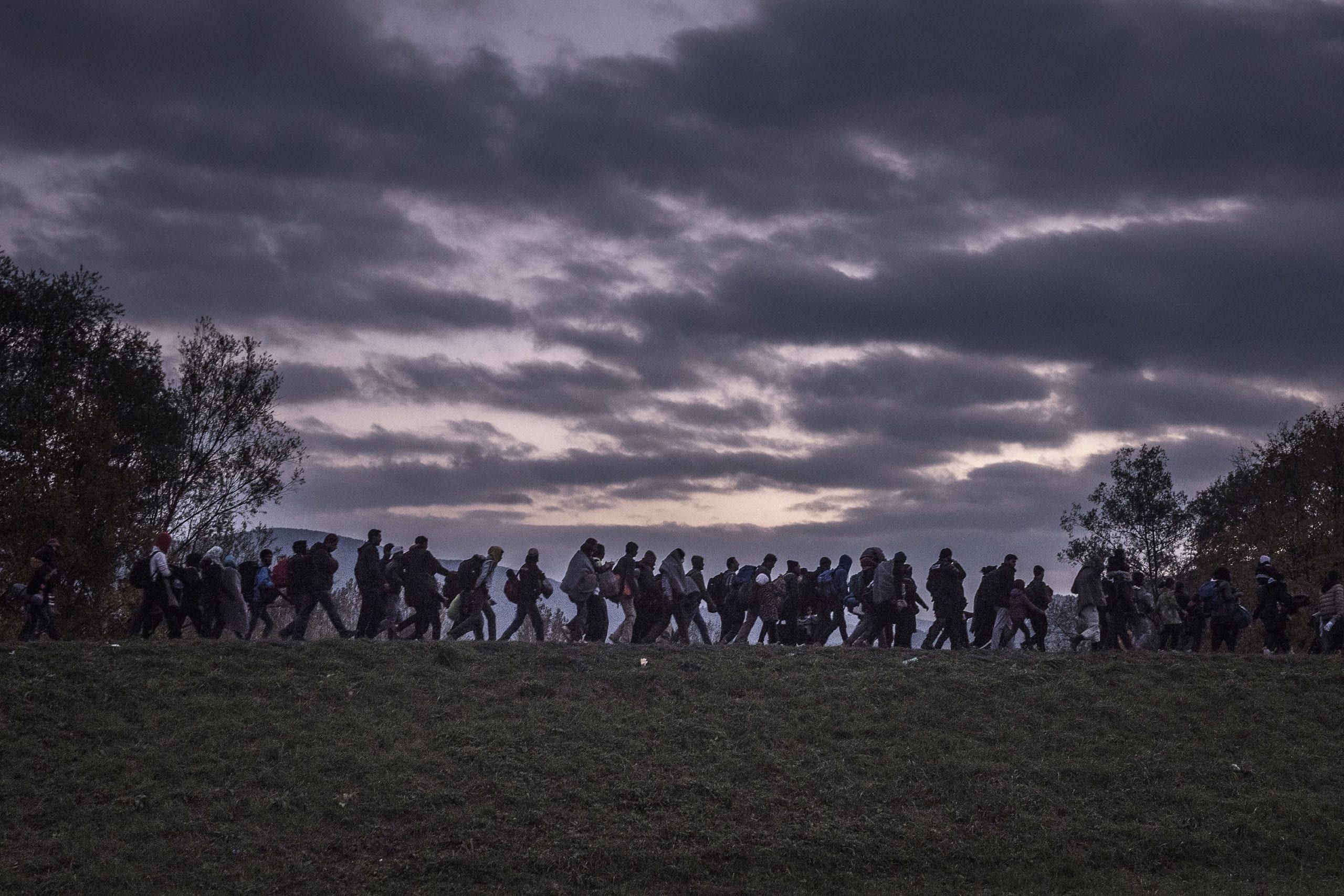 Migrants walked atop a dike as Slovenian riot police escorted them to a registration camp outside Dobova. War, drought and more are driving millions of people from their homelands © Sergey Ponomarev fo