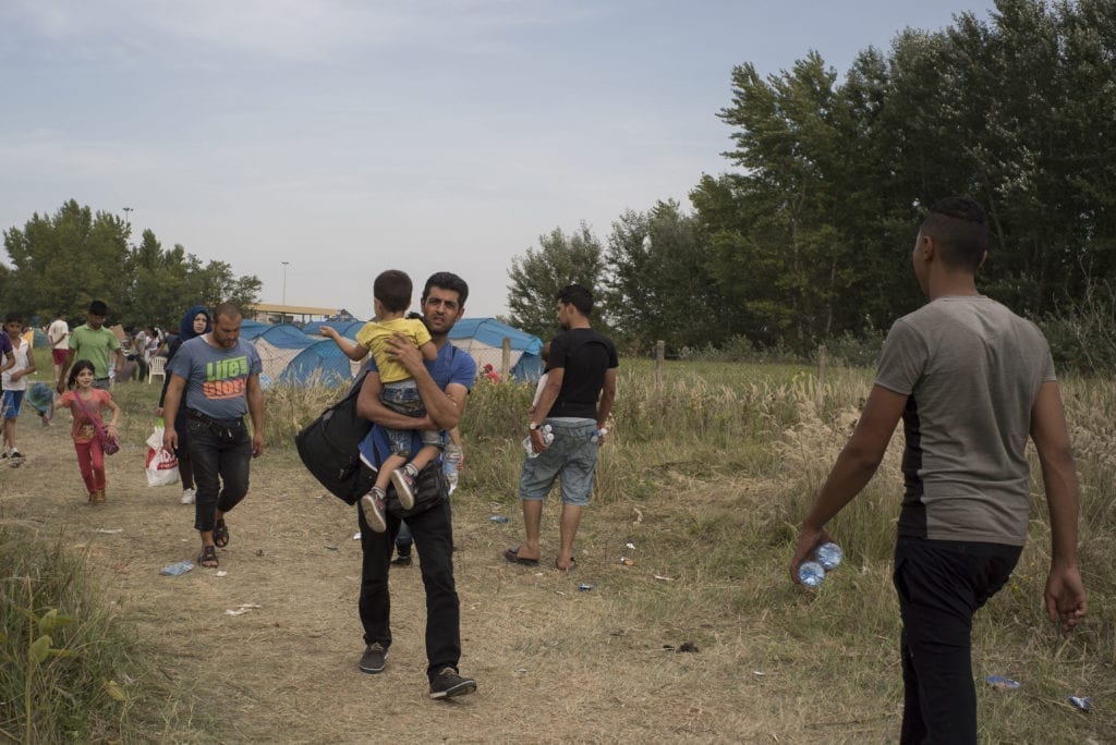 SERBIA, Horgos. September 16, 2015. Mohammed carries Brahim from the closed Serbian-Hungarian border after a rapid dash through Macedonia and Serbia. The border has closed at midnight the previous day, but Mohammed and the group hoped that it would be opened again. It quickly became clear that it wouldn't reopen and the next morning they left for Croatia.