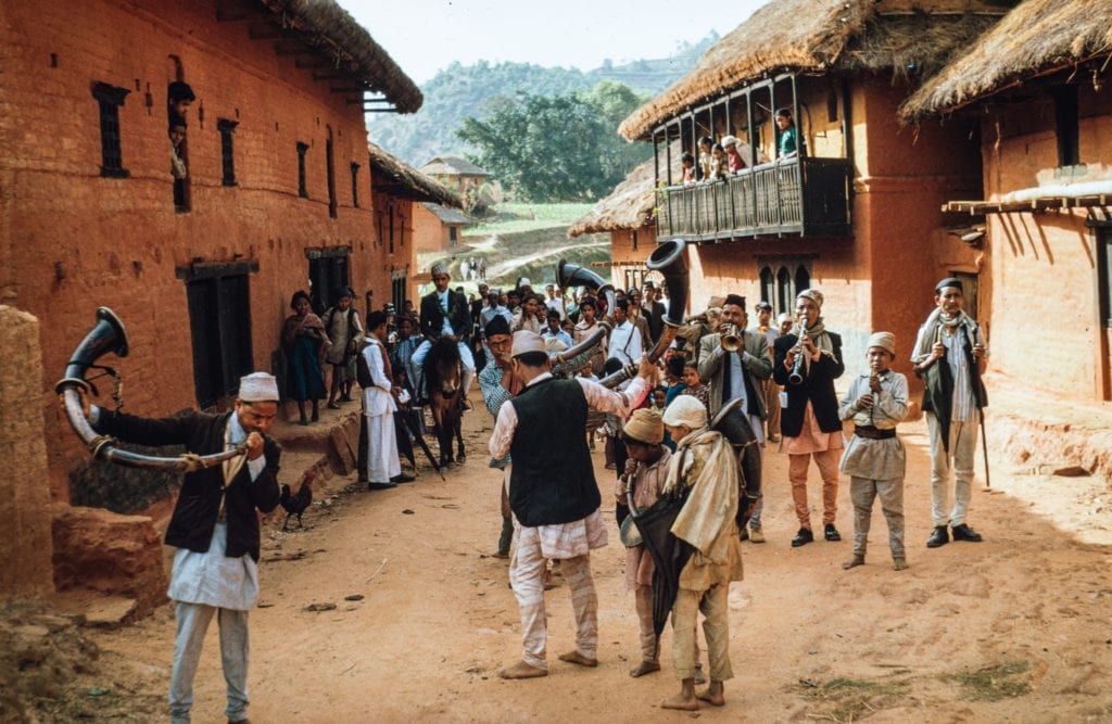 Date: 1964 Location: Bhojpur Description: A Damai ensemble leads a festival procession through a small village bazaar in Bhojpur district.