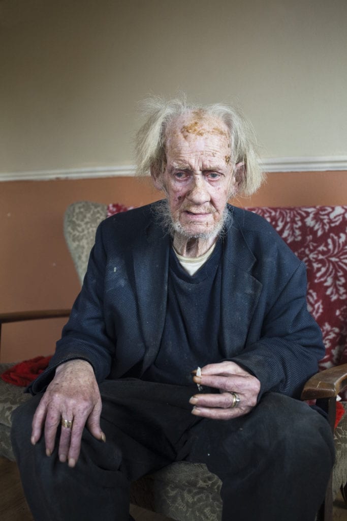 Old Jack is sitting in an old fashion armchair, smoking a cigarette at a haltingsite in County Carlow, Ireland.