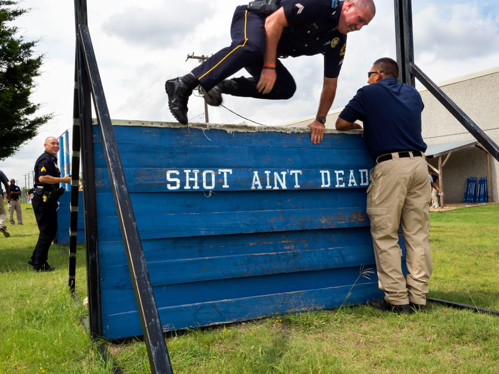 A Dallas Police Officer shows how to navigate the obsticle course to participants attending the basic class at the Dallas Junior Police Academy. Dallas is a major city in Texas and is the largest urban center of the fourth most populous metropolitan area in the United States. The city ranks ninth in the U.S. and third in Texas after Houston and San Antonio. The city's prominence arose from its historical importance as a center for the oil and cotton industries, and its position along numerous railroad lines. For two weeks in the summer of 2015, photographer Peter Dench visited Dallas to document the metroplex in his epic reportage, DENCH DOES DALLAS. Photographed using an Olympus E-M5 Mark II ©Peter Dench/Getty Images Reportage