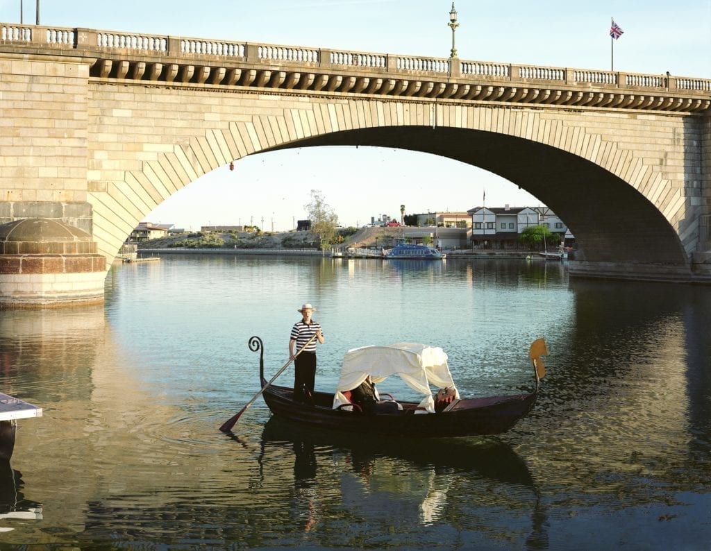 At a narrow point in the Thames River, Romans, who had recently invaded what is now modern day England, built a bridge. The year was 50 AD—the city of London grew up around that bridge. Over ensuing centuries, many replacement bridges have been built, each bearing the appellation ‘London Bridge.’ In the early 19th century, this stone bridge was built on the site. By the 1960s it was sinking into the muddy bottom of the Thames at a rate of 1 inch every 8 years. Not quite falling down, but enough to induce the city of London to sell the bridge. Piece by piece it was dismantled, brought to Lake Havasu, Arizona, and reassembled. Riding his bicycle over the bridge one day, David Jensen concluded that an Italian Gondola concession would go well with London Bridge. He built his gondola and proceeded to ply romantic tourists with arias in Italian, French, German, and Japanese. Image and text © Joel Sternfeld. Image courtesy of Luhring Augustine and Beetles+Huxley