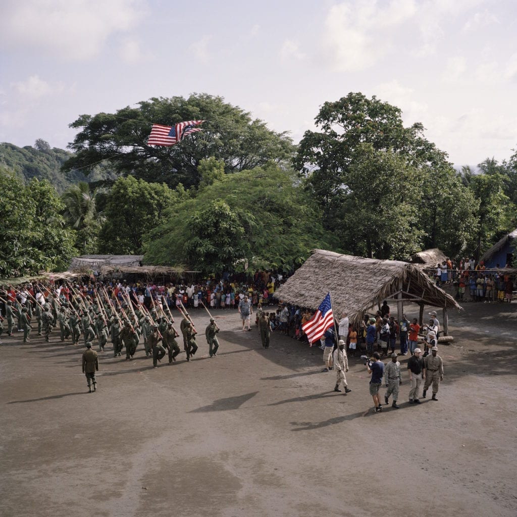 The John Frum Day celebrations on Tanna in February 2014. The villagers can be seen here marching with bamboo rifles as part of their annual ceremony, with Cevin, the American filmaker at the front of the line. From the series Cargo © Jon Tonks