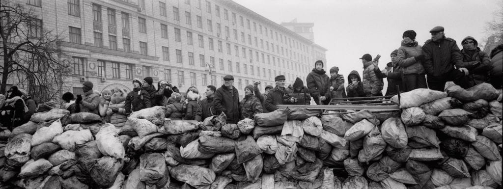 Ukrainian civilians stand behind a barricade as they watch at Riot police lines near the Maidan square in Kiev, 2014. Image © Pavel Wolberg, courtesy Prix Pictet