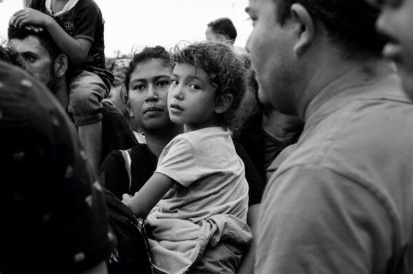 Chelita clings to her mother amidst the chaos of migrants waiting to be admitted into Mexico. After days of waiting at the border, Julio César Sánchez, the Director General of Special Affairs for the Secretariat of Foreign Affairs of the Federal Government of Mexico, appeared as a representative of the Mexican government. He began allowing families to enter in small groups after making ambiguous promises that didn't apply to all members of the caravan. He never said what would happen to the families or where they would be taken.